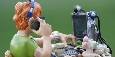 Proslinsfigur av en programmerare som sitter och kodar med två skärmar och två tangentbord samtidigt som hen talar i telefon.